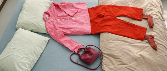 Look montado sobre a cama: camisa rosa, calça vermelha e bolsa vinho